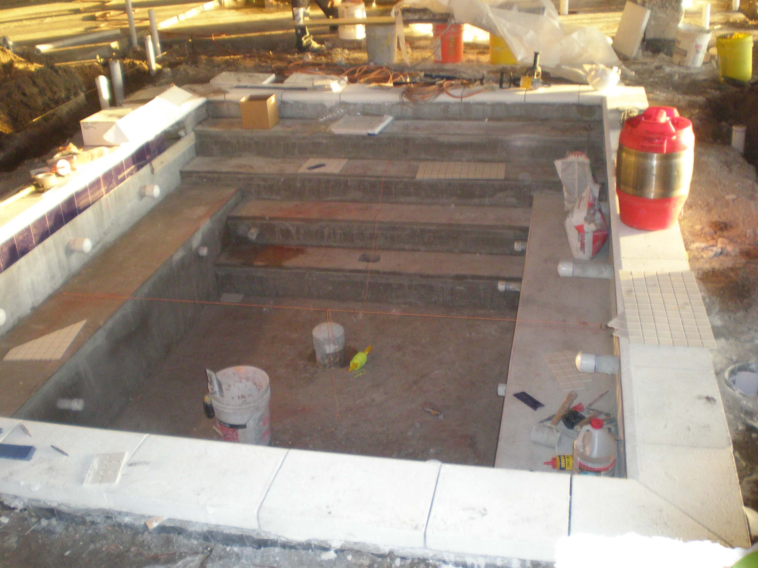 Swimming pool under construction with initial tile prep work in progress, showing steps and surrounding areas ready for tiling.