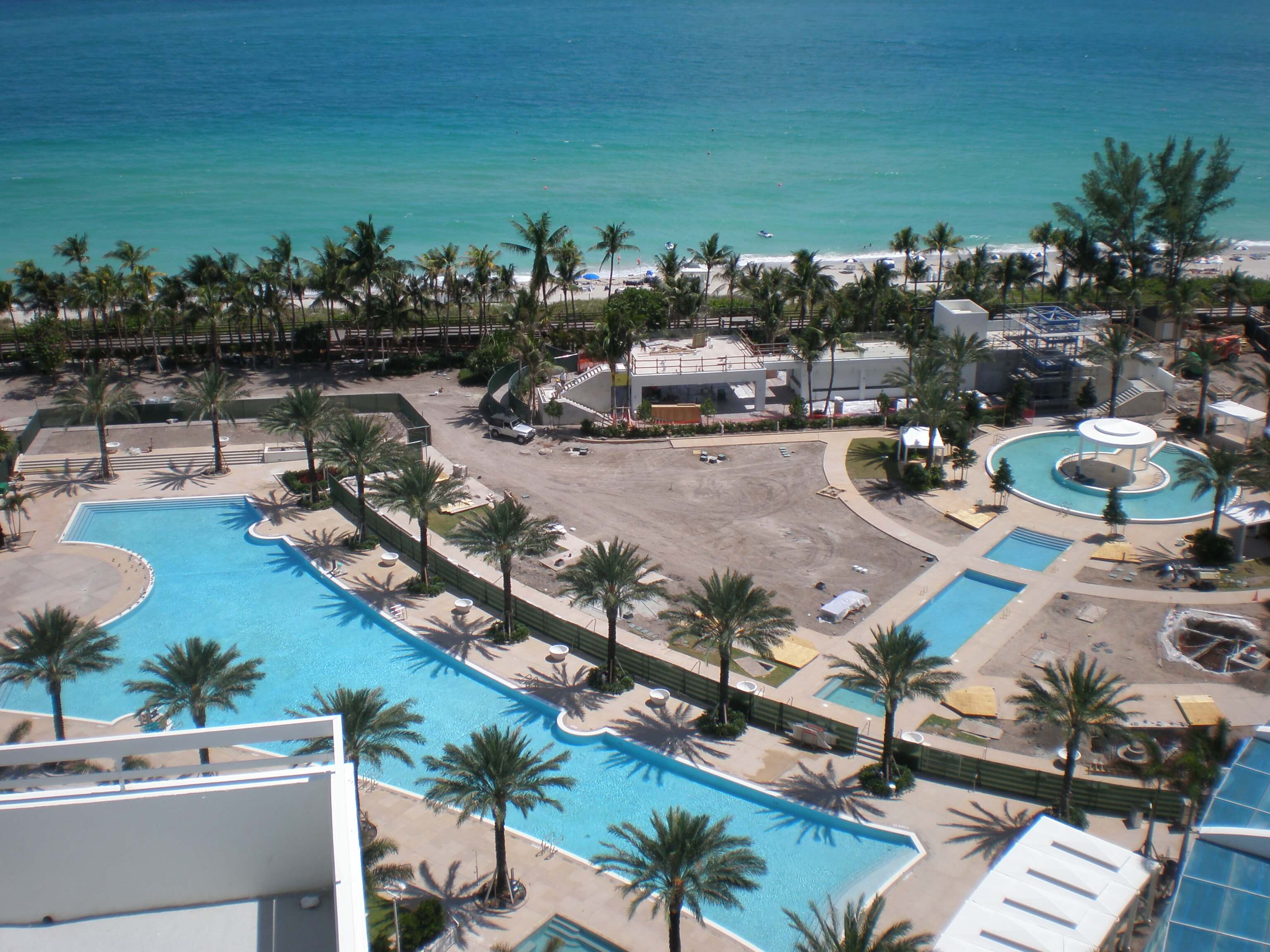 Aerial view of a luxury pool area under construction near the ocean, with palm trees and the beach in the background at the Fontainebleau Miami Beach resort.