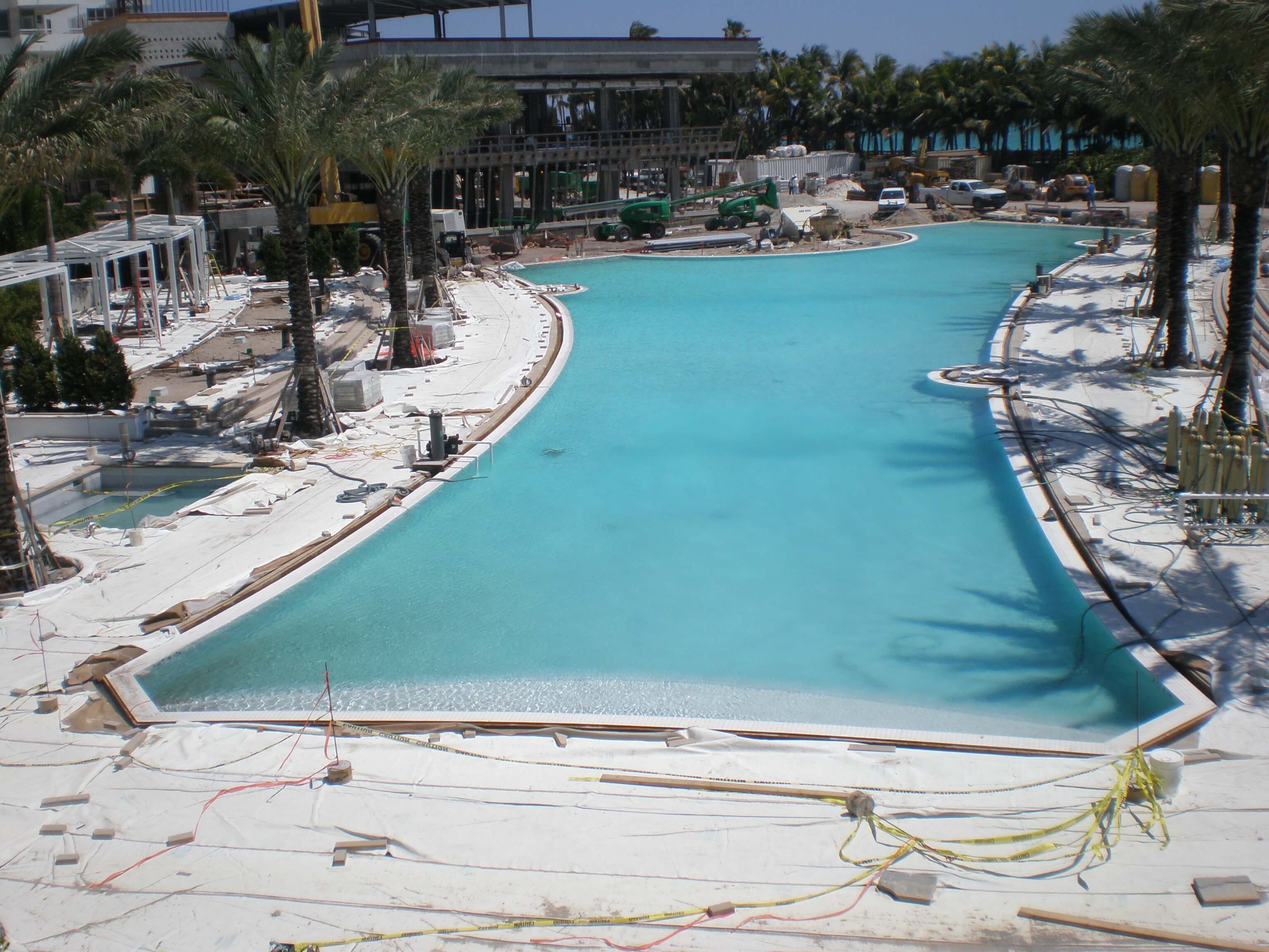 Construction progress of a large pool at the Fontainebleau Miami Beach resort, showing the pool surrounded by construction materials and equipment.