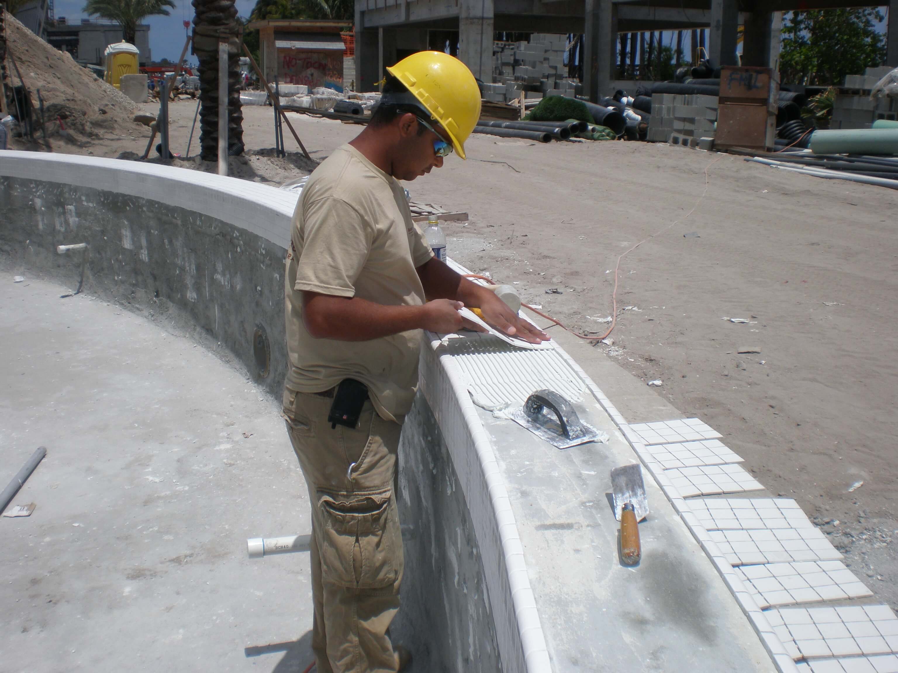 Tile installer carefully placing small mosaic tiles along the curved edge of a pool wall during construction at the Fontainebleau Miami Beach resort.