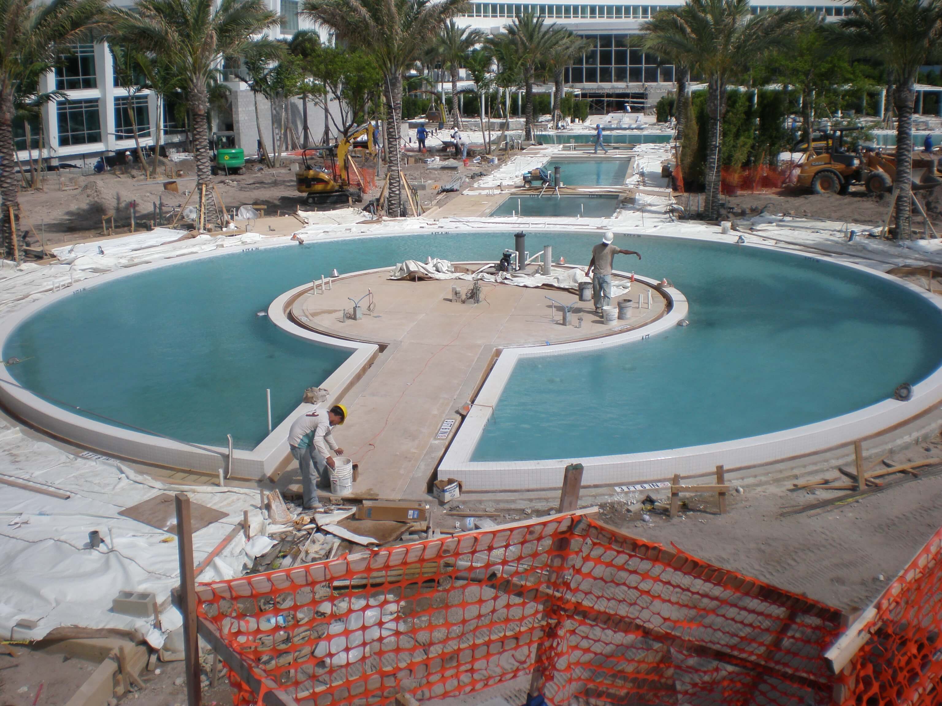 Construction workers finishing the installation of tiles around a large circular pool at the Fontainebleau Miami Beach resort, surrounded by construction materials and equipment.