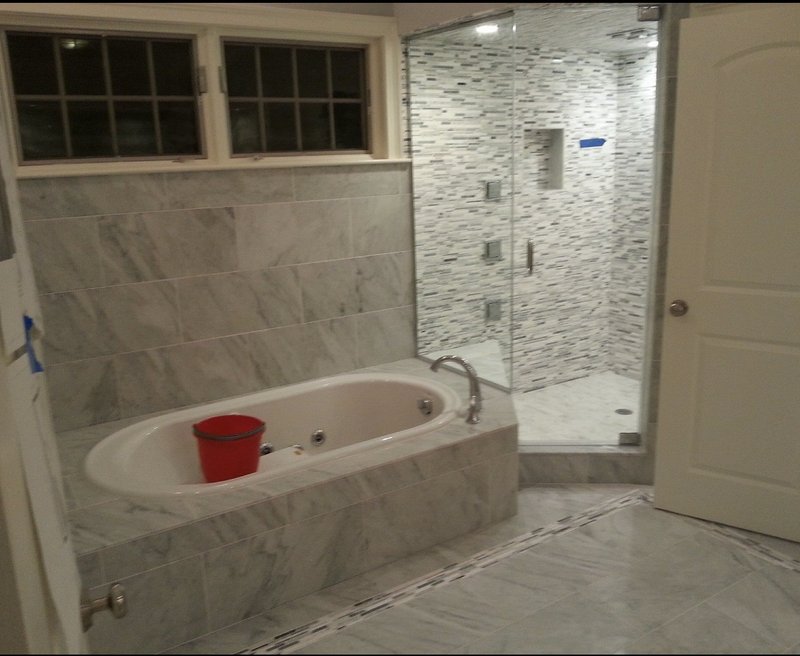 Marble bathroom featuring a soaking tub and a glass-enclosed shower with mosaic tiles.