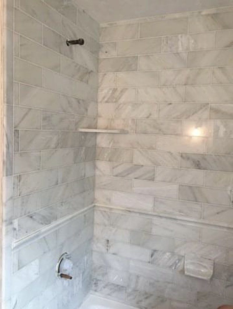 Elegant marble-tiled shower with subway-style tiles and a built-in shelf.