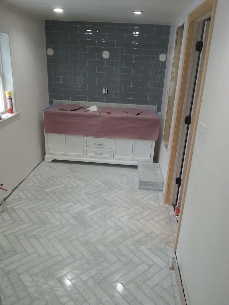 Bathroom renovation with herringbone-patterned marble floor and gray subway tile backsplash.