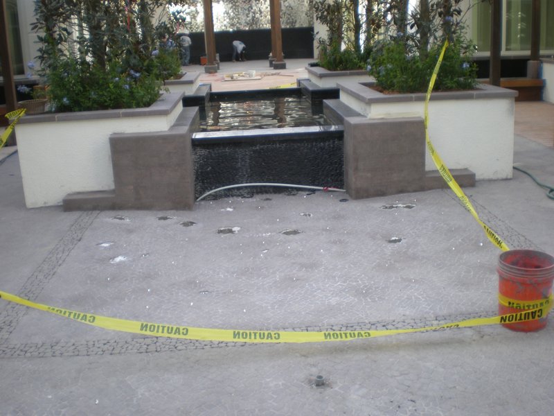Water feature under construction with caution tape around the area, showing a partially completed tiled surface.