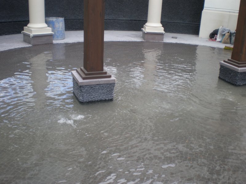 Water feature with tiled surface and wooden pillars, partially filled with water.