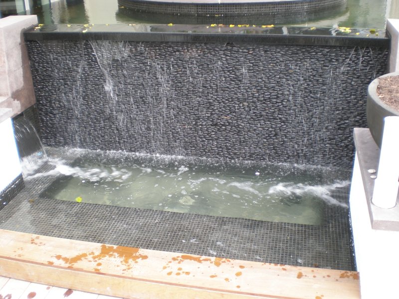 Completed water feature with black pebble tiles and cascading water, surrounded by other water elements.