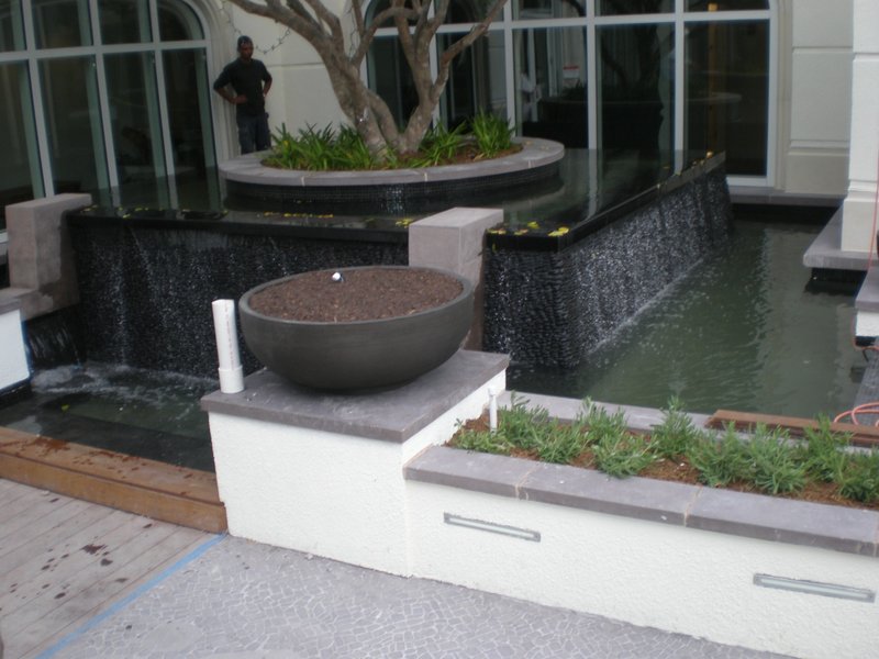 Completed water feature with cascading water and planters, surrounded by tiled surfaces in an outdoor space.
