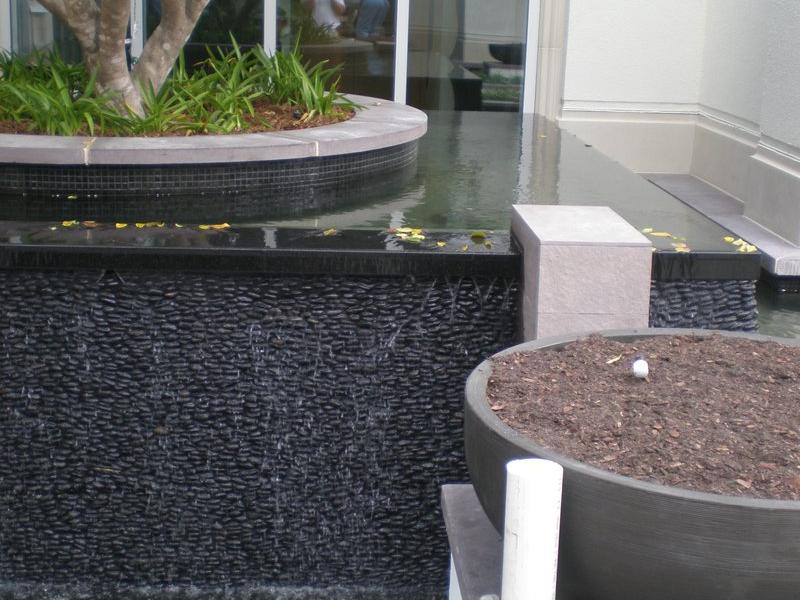 Tiled planter feature with water flowing into an adjacent water basin, part of a larger water installation.